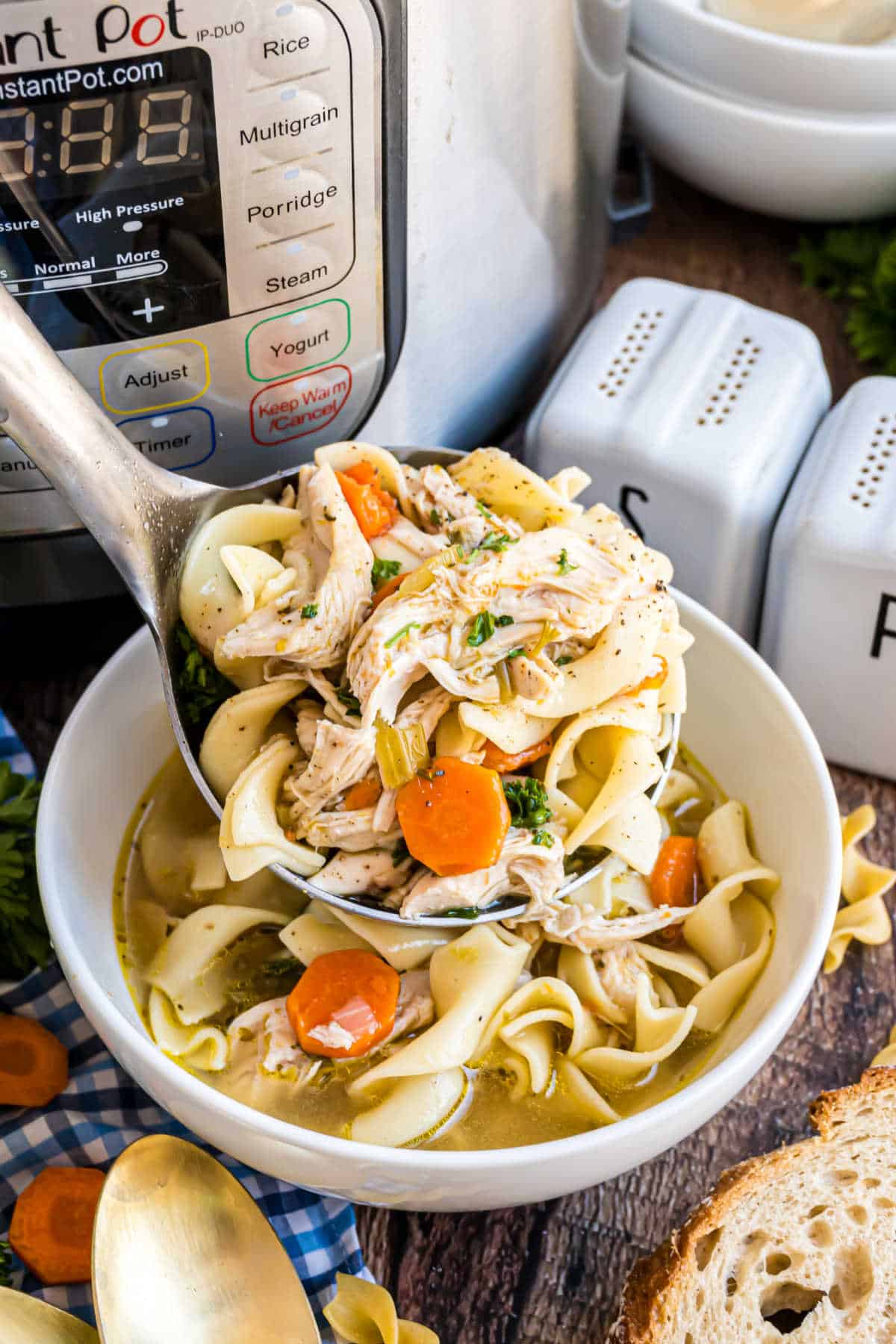 A ladle of hearty chicken noodle soup with carrots and herbs is being served from an Instant Pot into a white bowl.