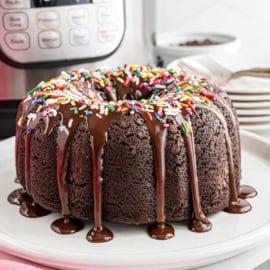 Instant pot chocolate bundt cake with chocolate glaze and rainbow sprinkles on a white plate.