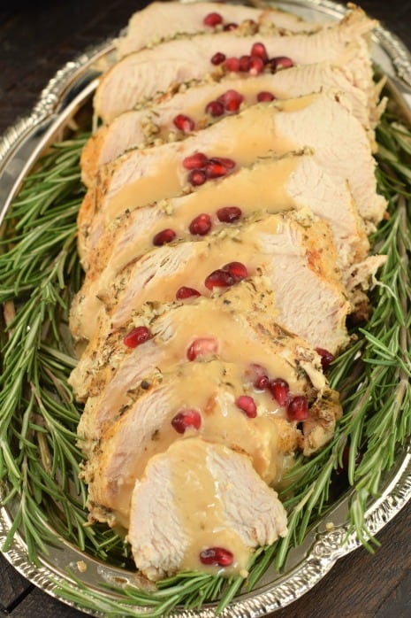 Turkey breast on platter with rosemary, gravy, and pomegranate seeds.
