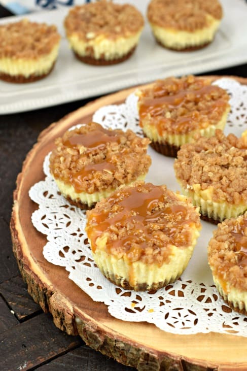 Caramel apple cheesecakes on a white doily on a wooden cake plate.