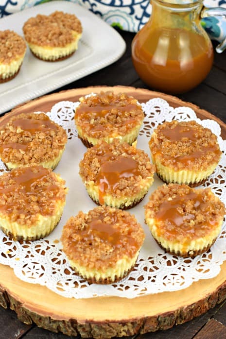 Caramel apple cheesecakes on a wooden cake plate with white doily.