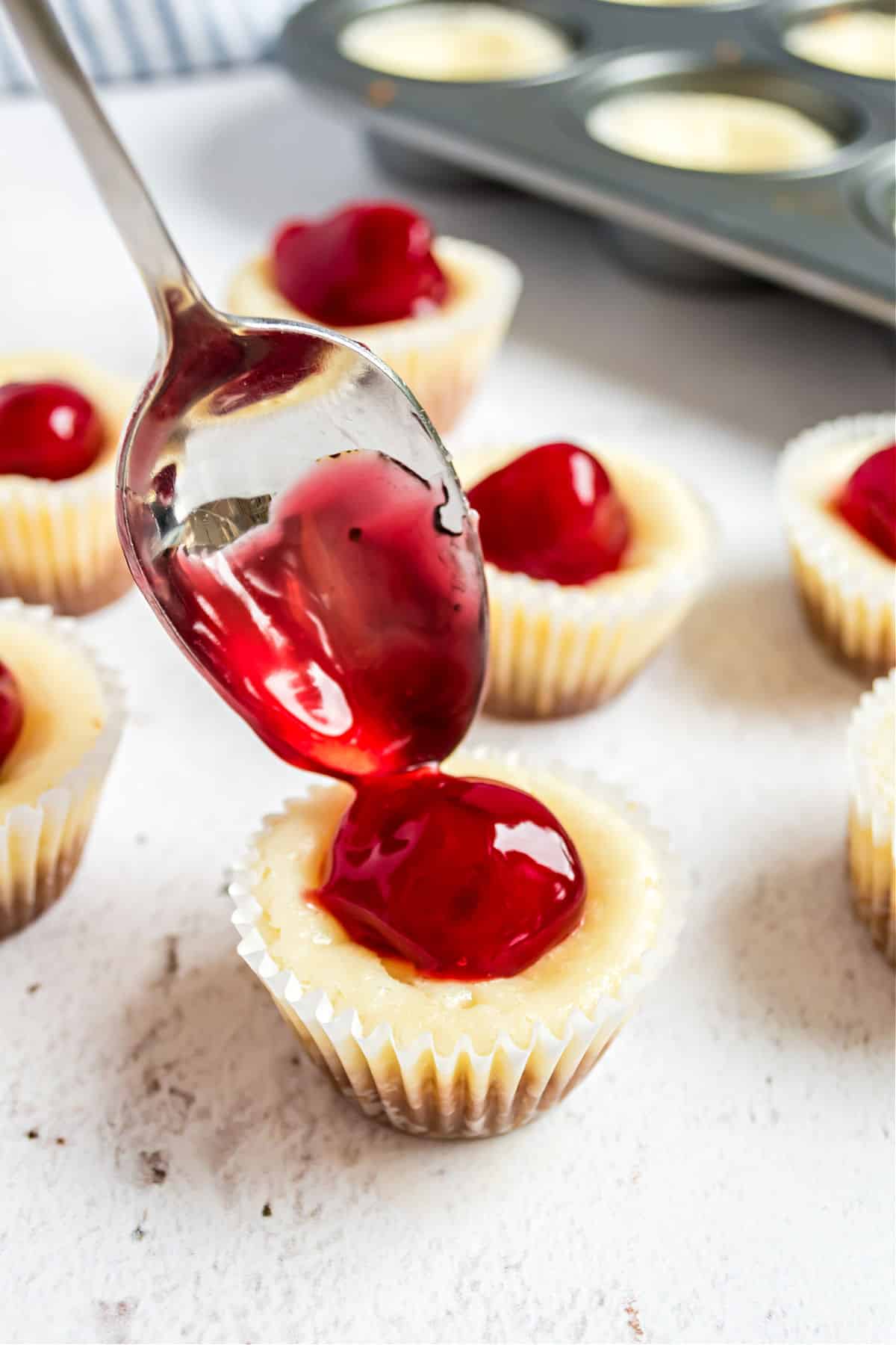 Cherry pie filling being spooned onto a mini cheesecake.