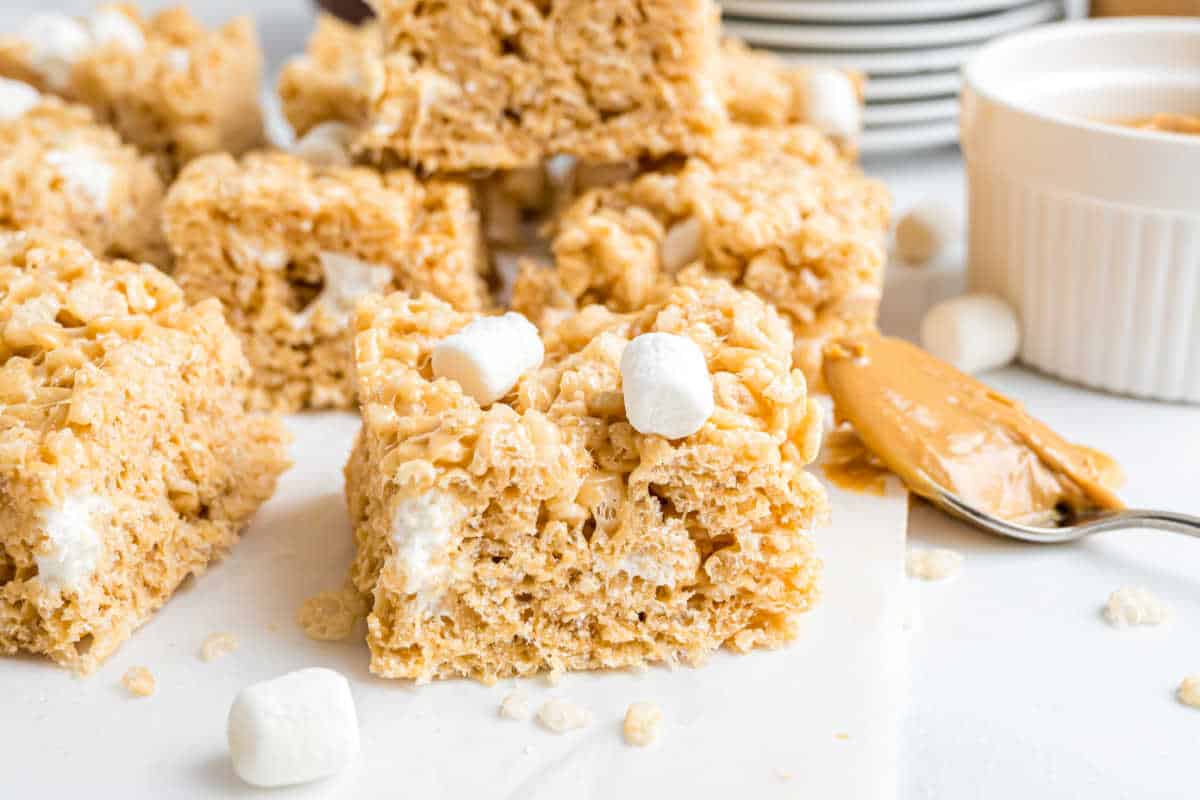 Close-up of peanut butter rice krispie treats with mini marshmallows and a spoonful of creamy peanut butter nearby.