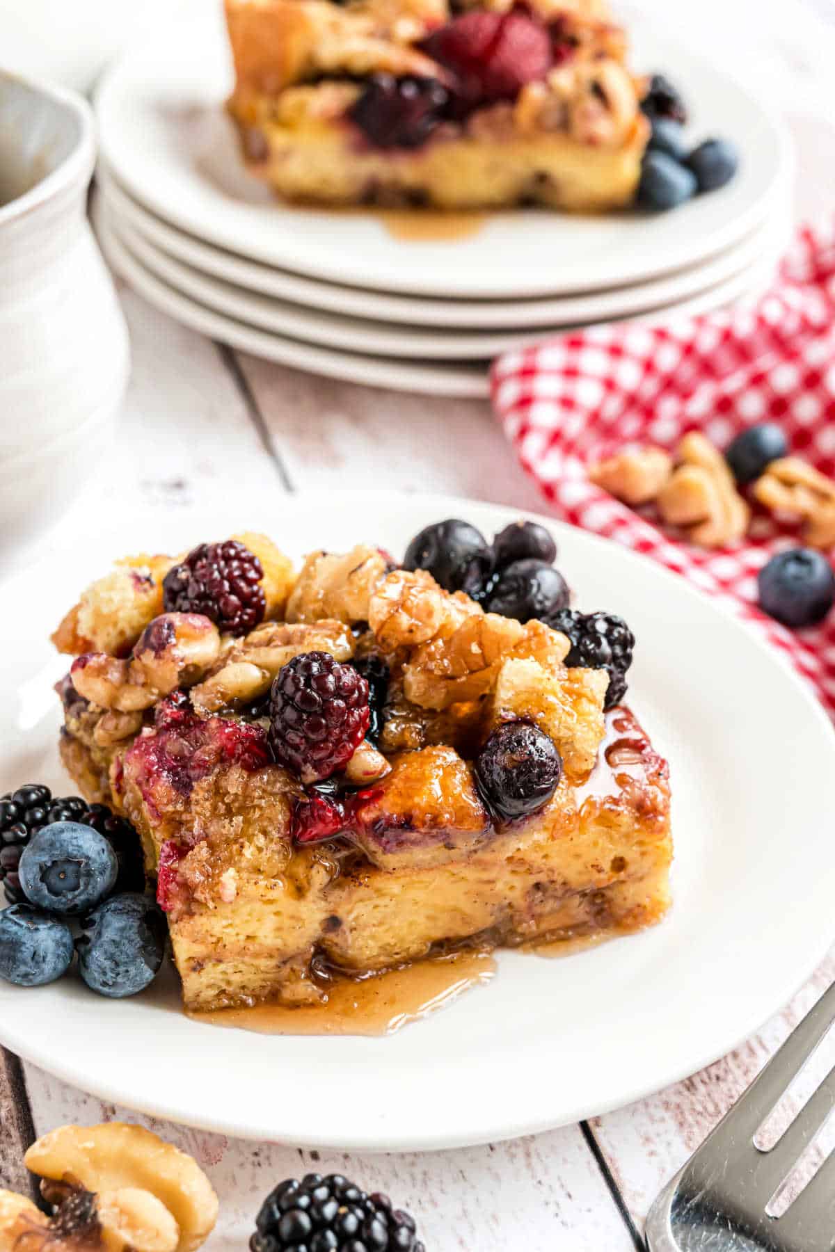 Slice of french toast casserole with berries and syrup on a white plate.