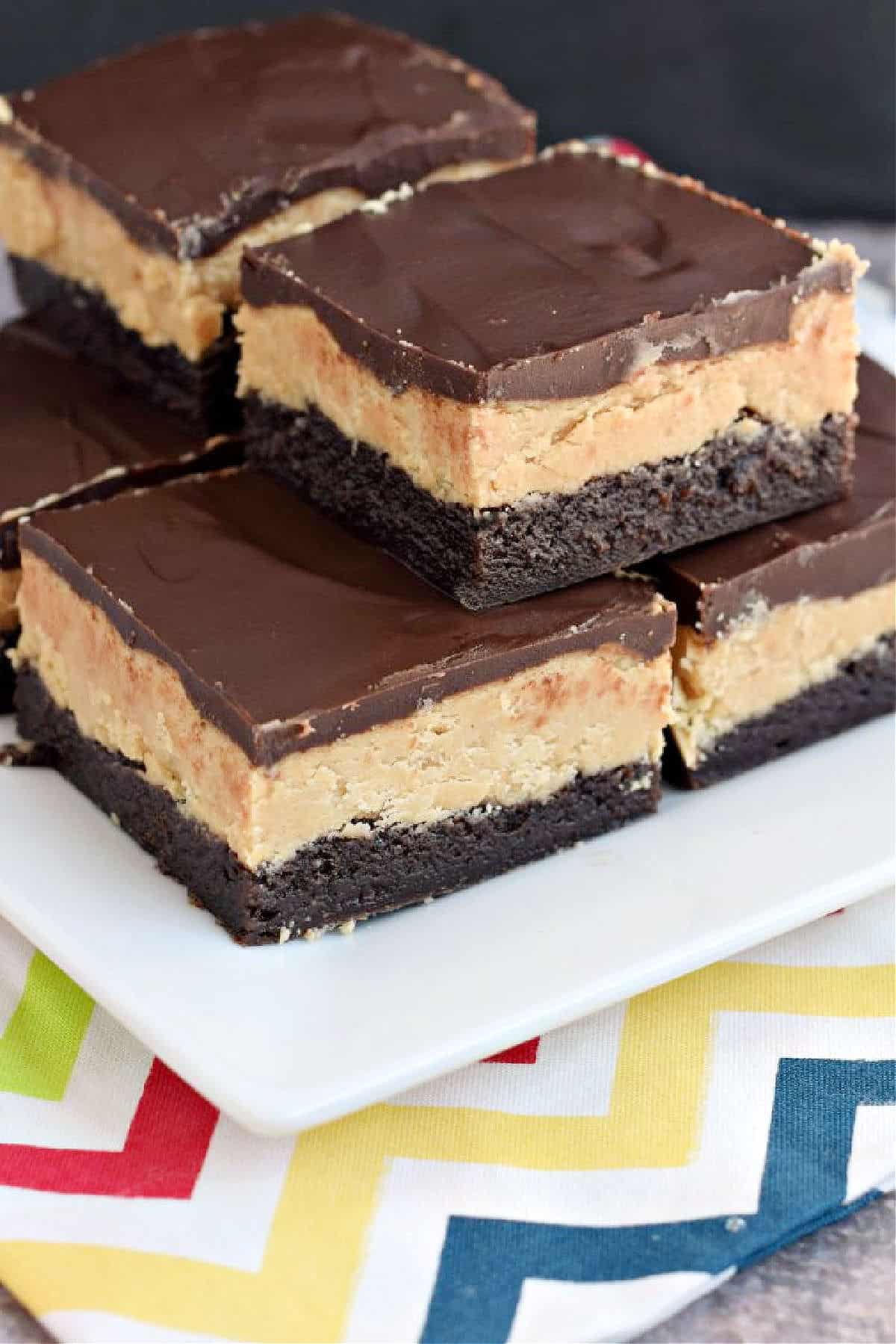 Stack of brownies topped with peanut butter filling and ganache on a white plate.