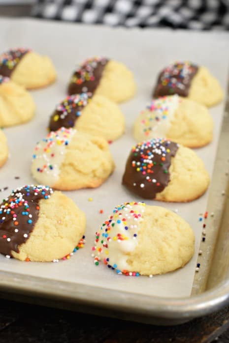 Metal baking sheet with parchment paper and butter cookies dipped in chocolate and white chocolate with sprinkles.