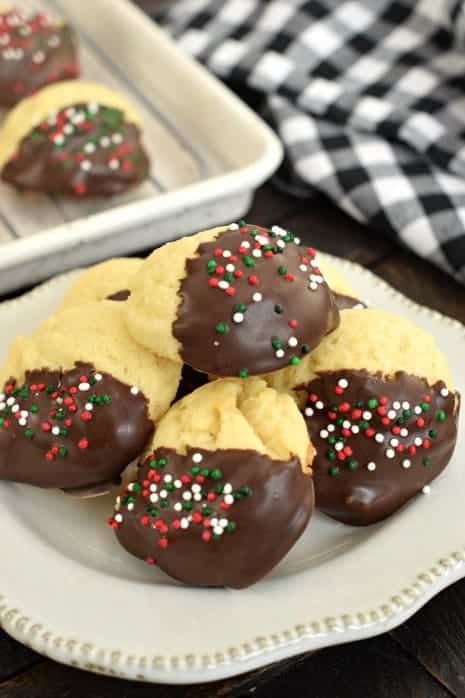 Soft butter cookies dipped in chocolate on a white plate with a black and white checked napkin in background.