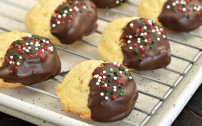 Wire cooling rack with butter cookies dipped in dark chocolate and holiday sprinkles.