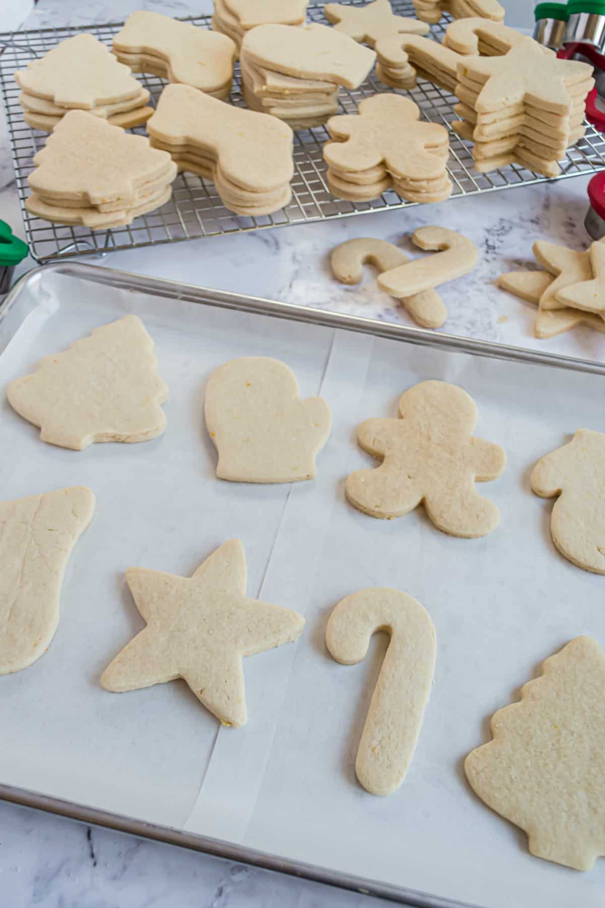 Unfrosted sugar cookies in christmas shapes on parchment paper and wire rack.