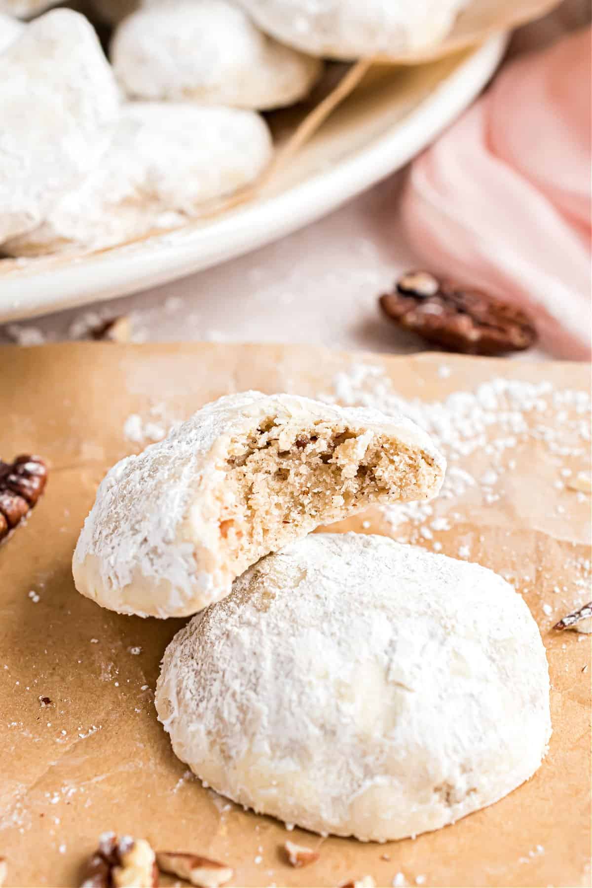 Cookies with powdered sugar on parchment paper, and one bite taken out.