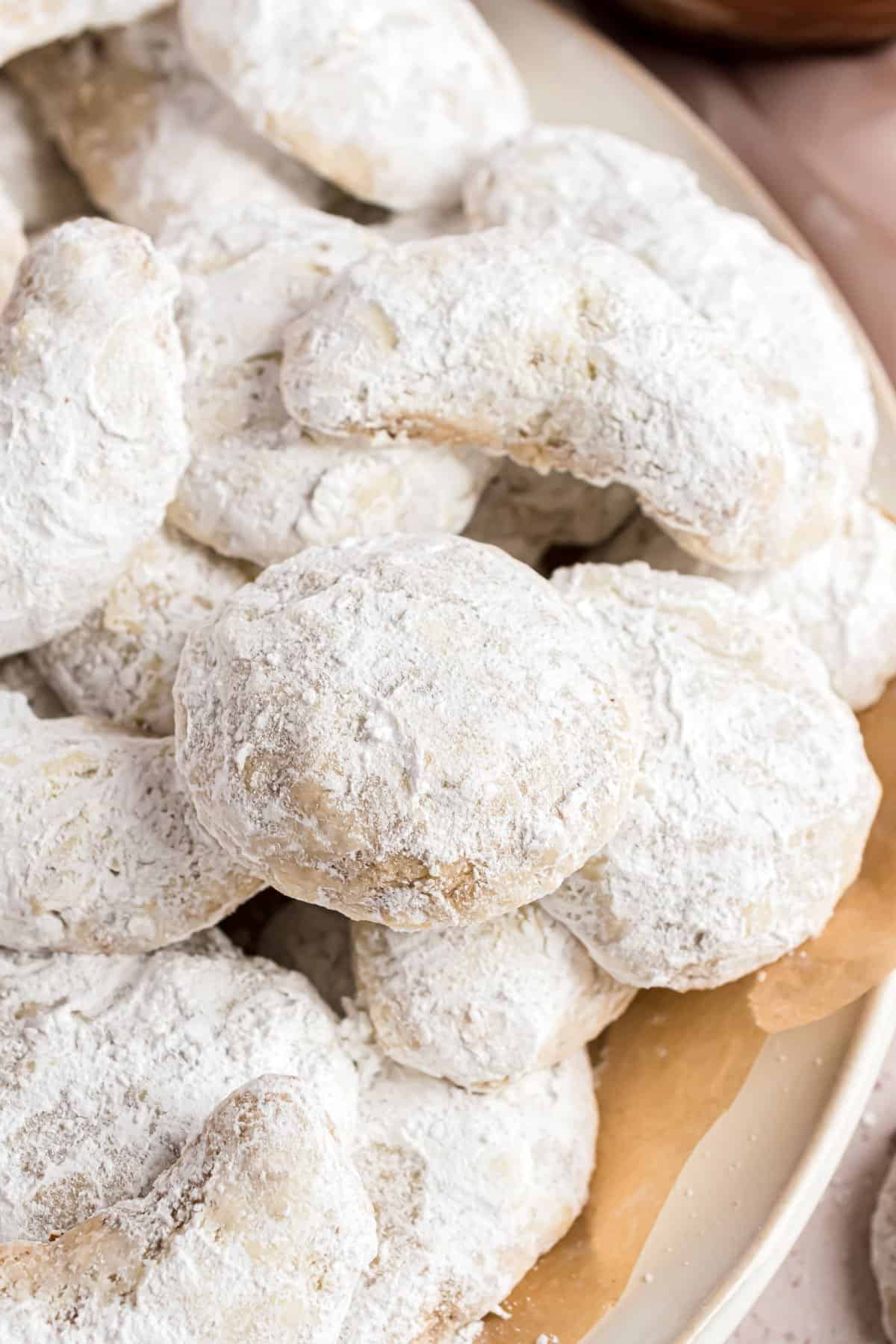 Snowball cookies stacked on parchment paper lined cookie sheet.