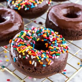 Chocolate donuts baked and cooled on wire rack with sprinkles.