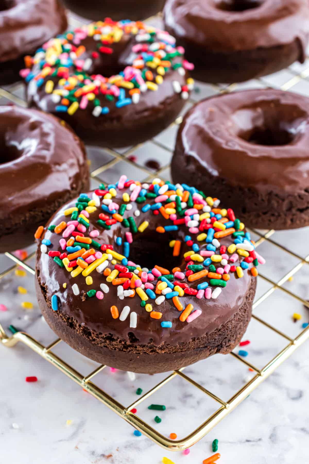 Chocolate donuts baked and cooled on wire rack with sprinkles.