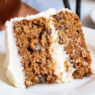 Slice of carrot cake with cream cheese frosting on white plate.