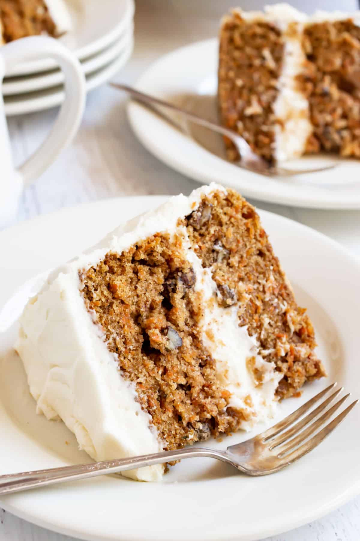 Two slices of carrot cake with cream cheese frosting on white plates.