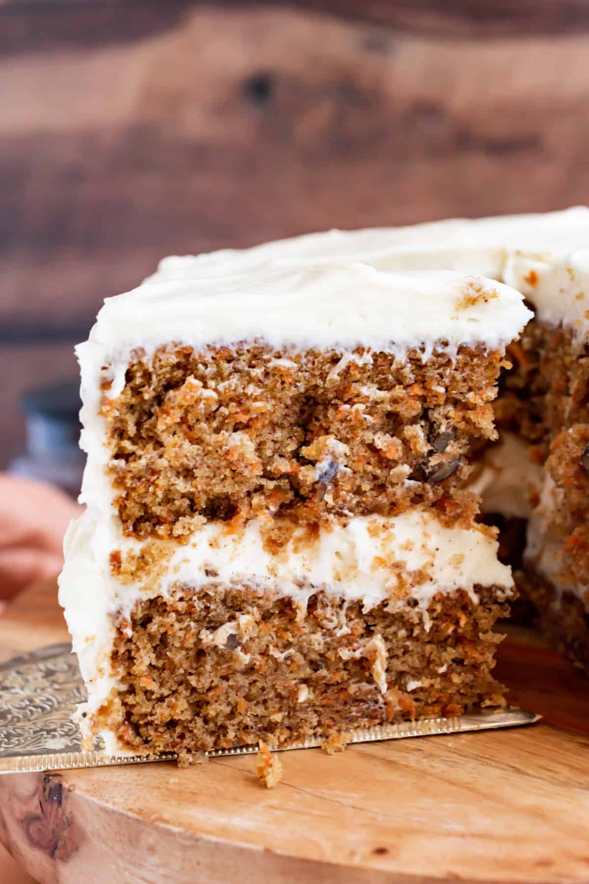 Double layer carrot cake with cream cheese frosting on a wood cake platter.