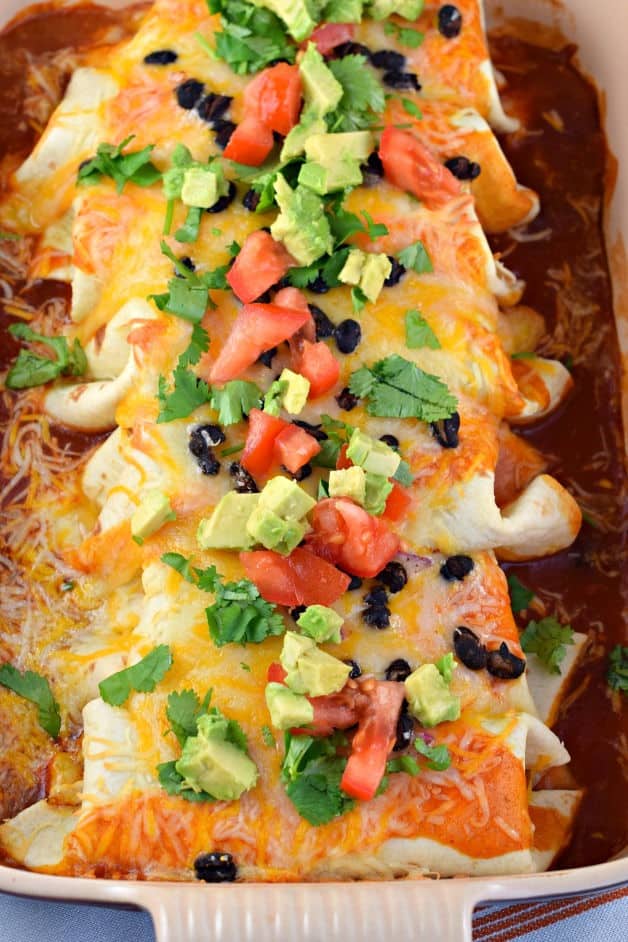 Chicken enchiladas stuffed with avocado and beans and topped with fresh vegetables.