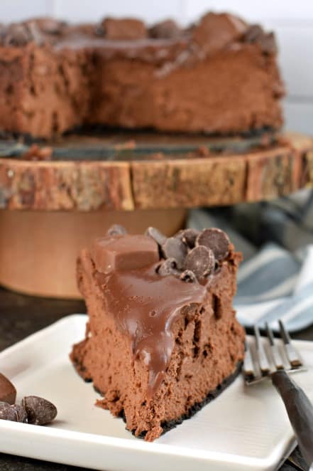 Slice of chocolate cheesecake on a white plate, topped with ganache.