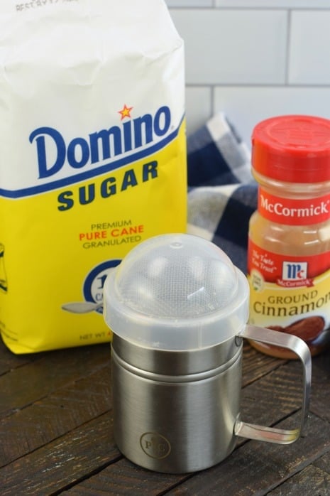 Bag of sugar, shaker of cinnamon, and a silver container to combine them in.
