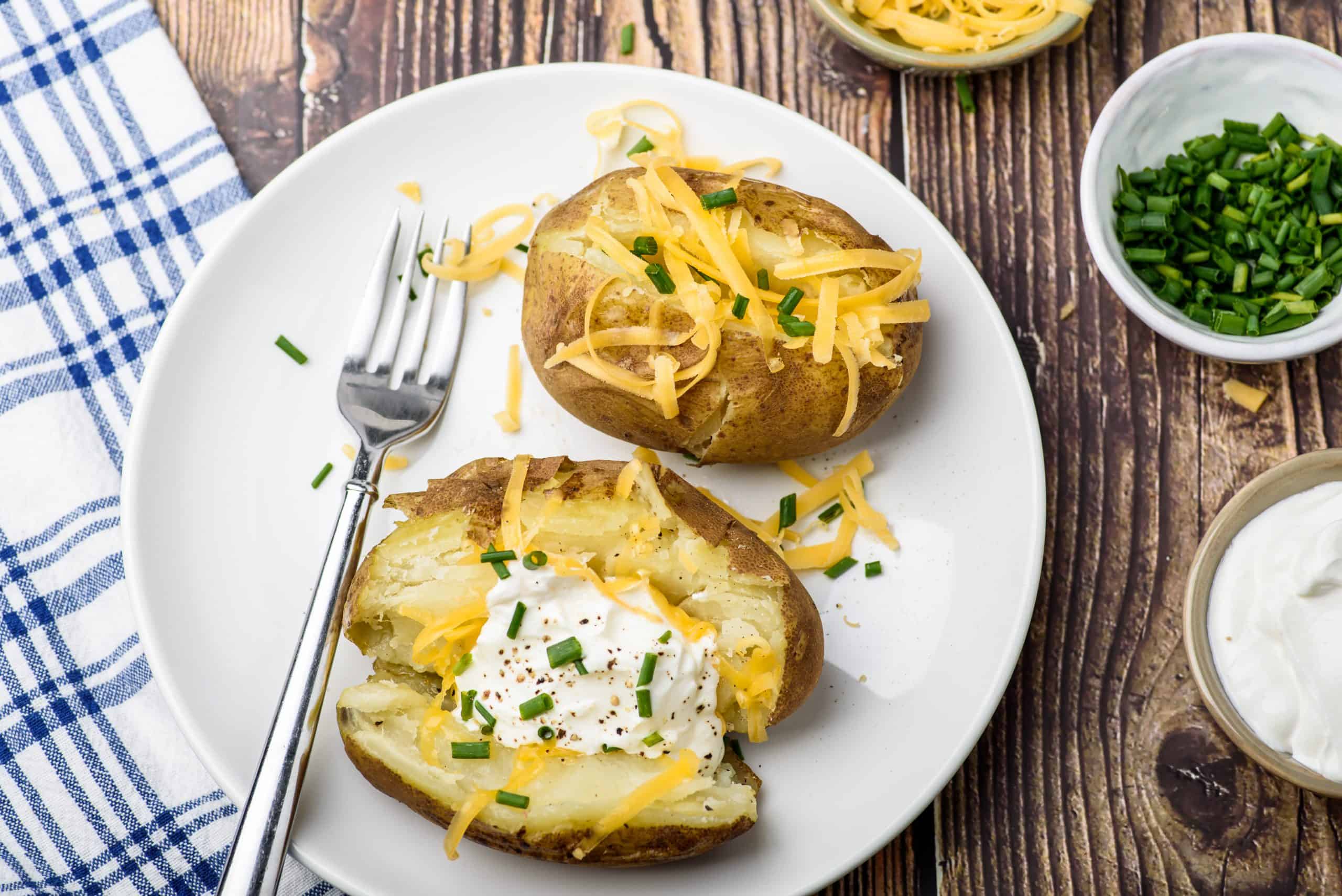 Dinner plate with baked potatoes topped with cheese and sour cream.