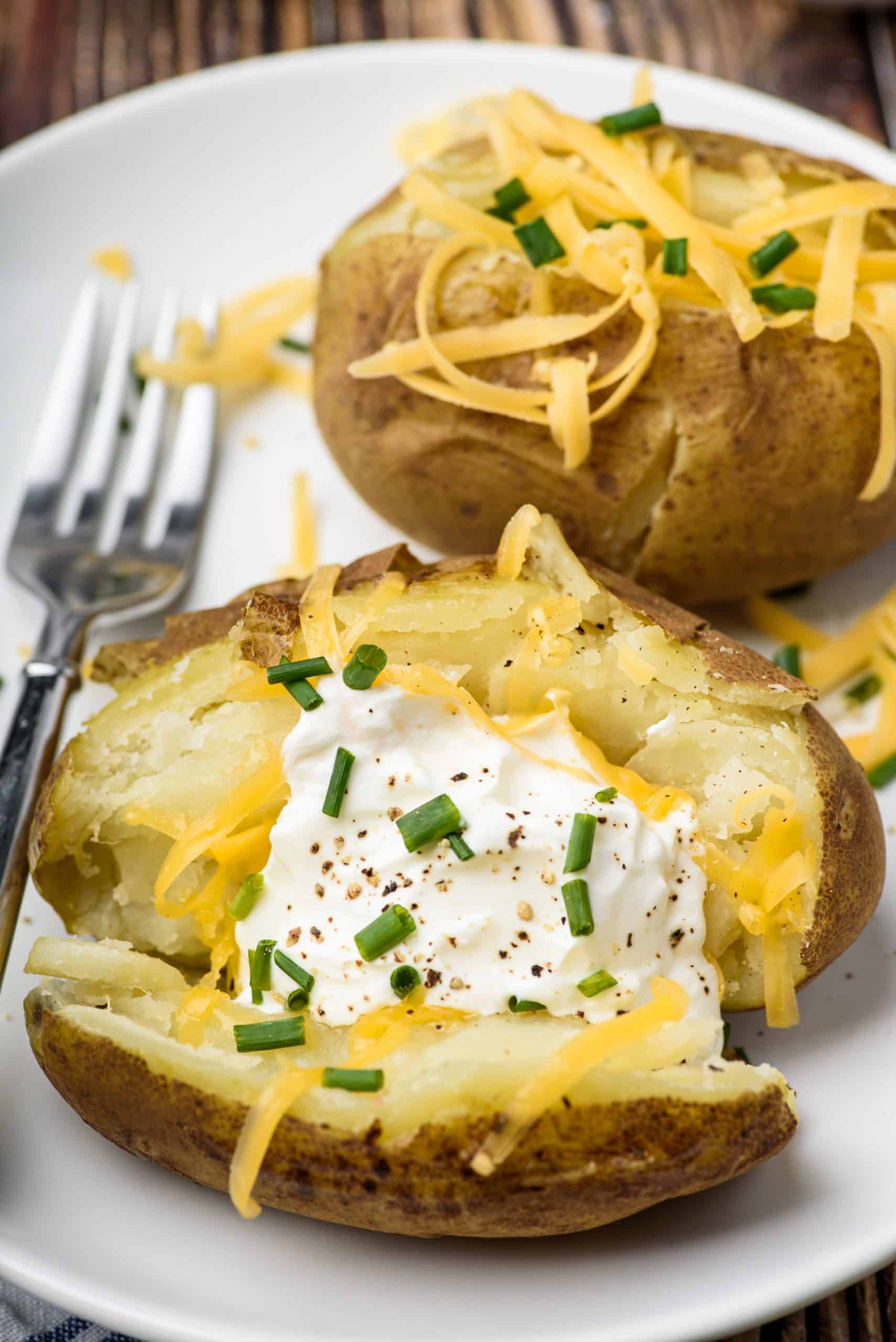 Baked potatoes open in half and topped with sour cream, cheese, and chives.