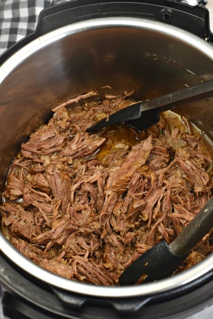 Instant Pot with beef barbacoa, shredded and tongs to serve.