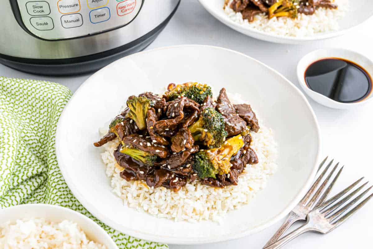 Instant Pot beef broccoli served over rice in a white bowl, with savory soy sauce and the Instant Pot in the background.