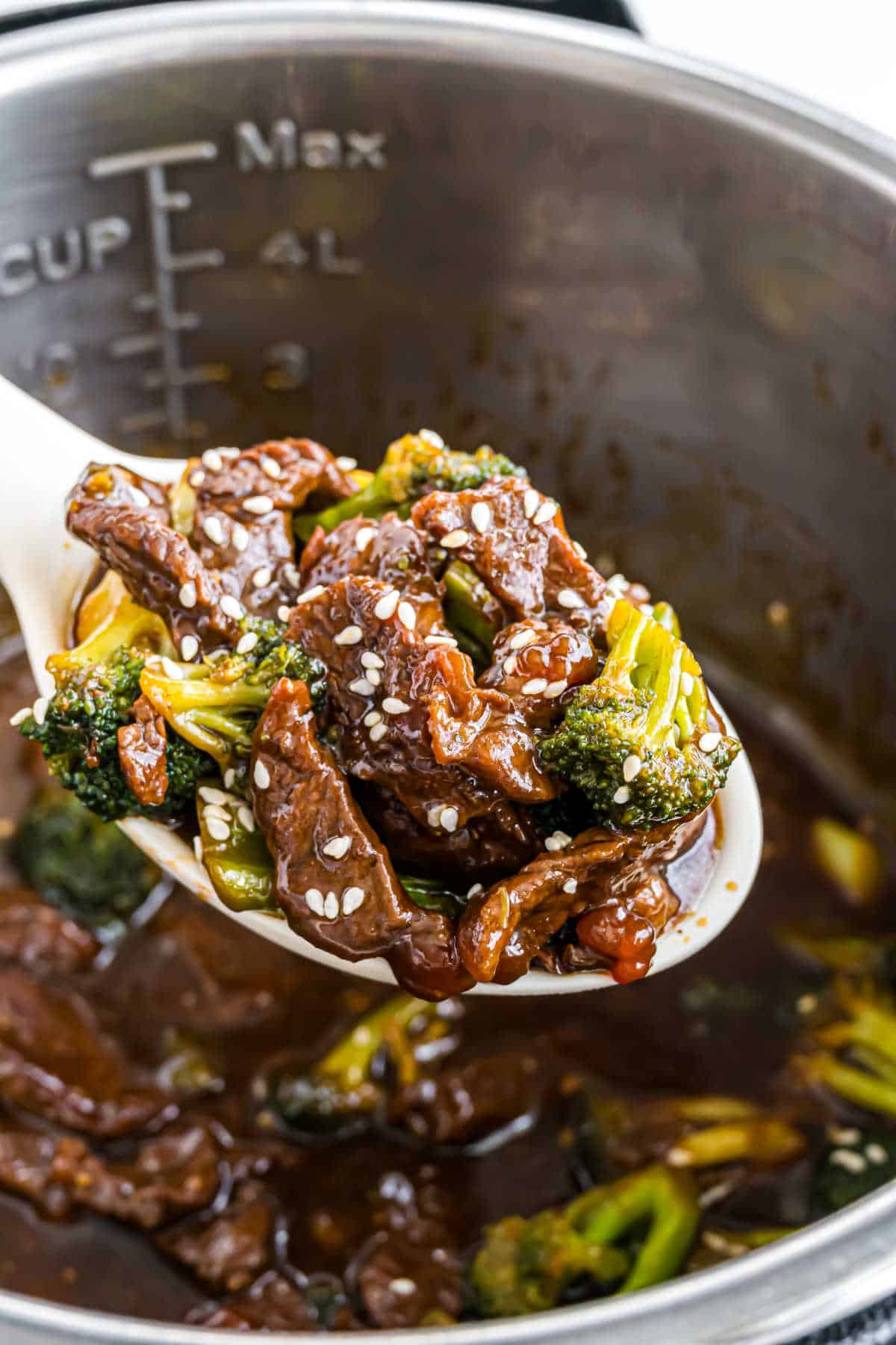 A spoonful of Instant Pot beef broccoli in savory sauce, topped with sesame seeds, held over a metal pot.