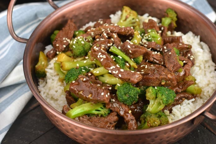 Copped skillet with white rice and beef broccoli garnished with sesame seeds.