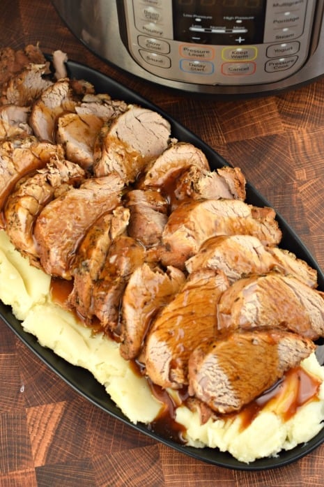 Plate of sliced pork tenderloin on pile of mashed potatoes with balsamic glaze. Instant Pot in background.