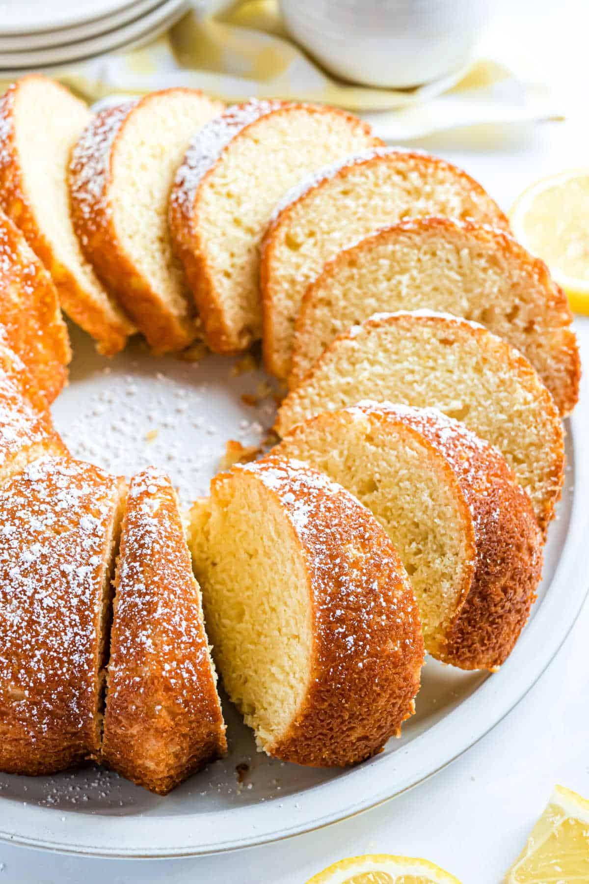 Lemon bundt cake cut into slices on a white platter.