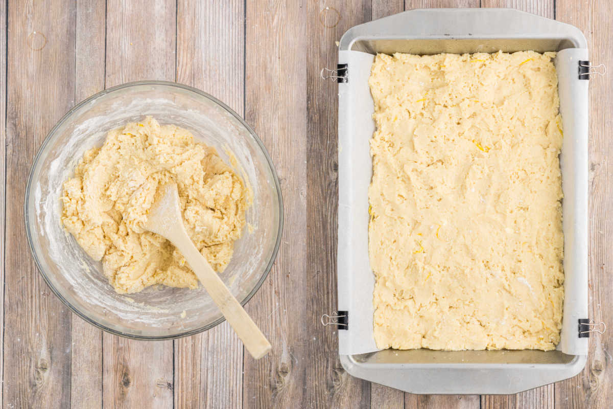 A bowl of dough with a wooden spoon sits next to a baking pan of lemon cake bars on a wooden surface.