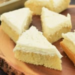 Triangular pieces of frosted shortbread, reminiscent of lemon cake bars, elegantly arranged on a wooden platter.