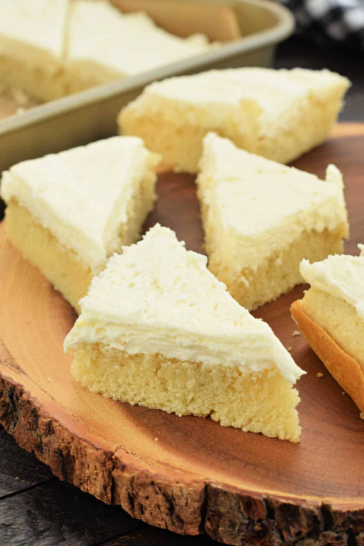 Triangular vanilla cake slices with frosting rest elegantly on a wooden platter, reminiscent of delightful lemon cake bars.