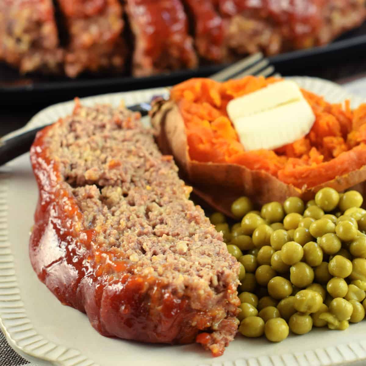 Meatloaf with glaze served on a plate with peas and sweet potato.