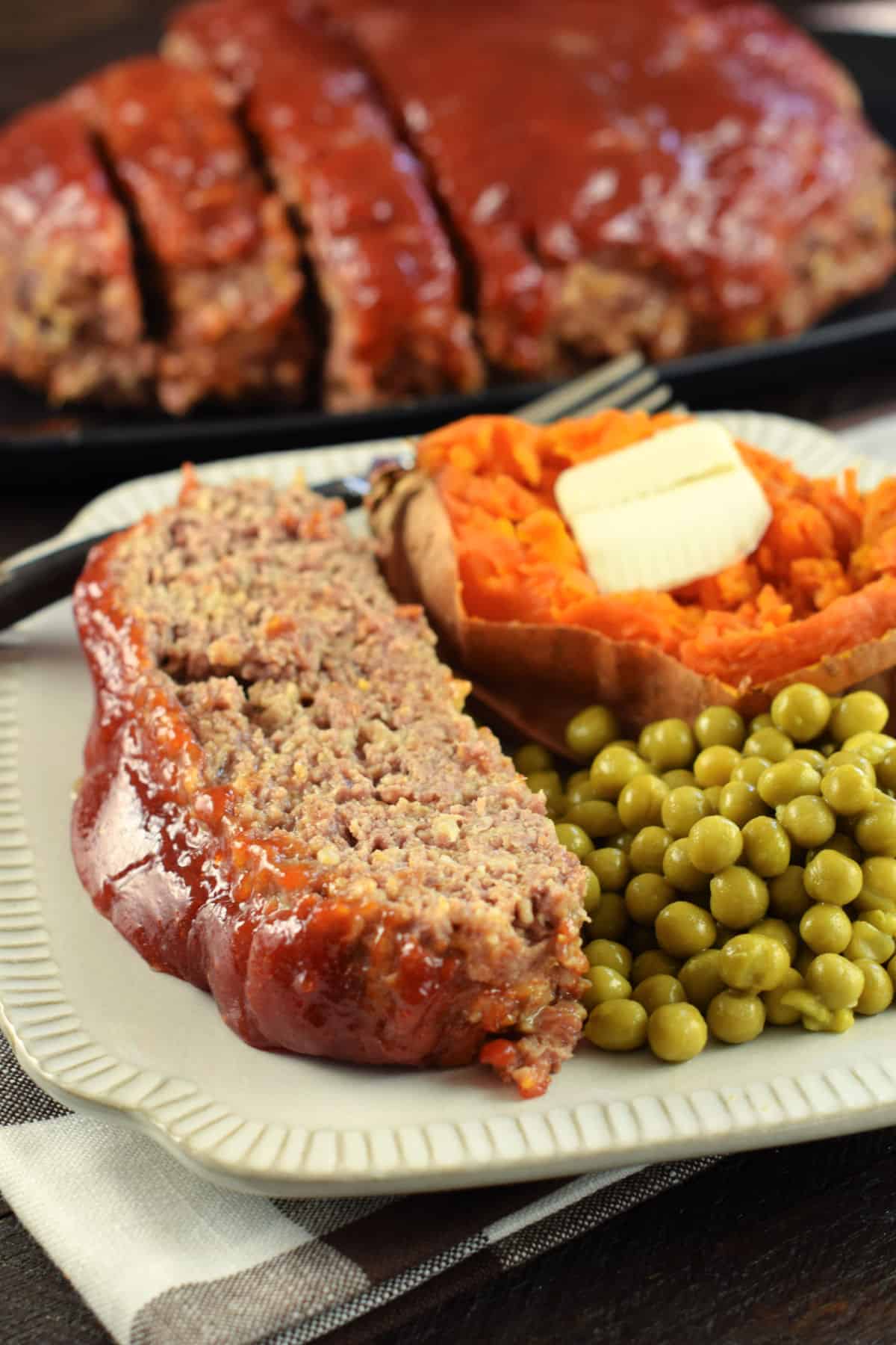 Meatloaf with glaze served on a plate with peas and sweet potato.