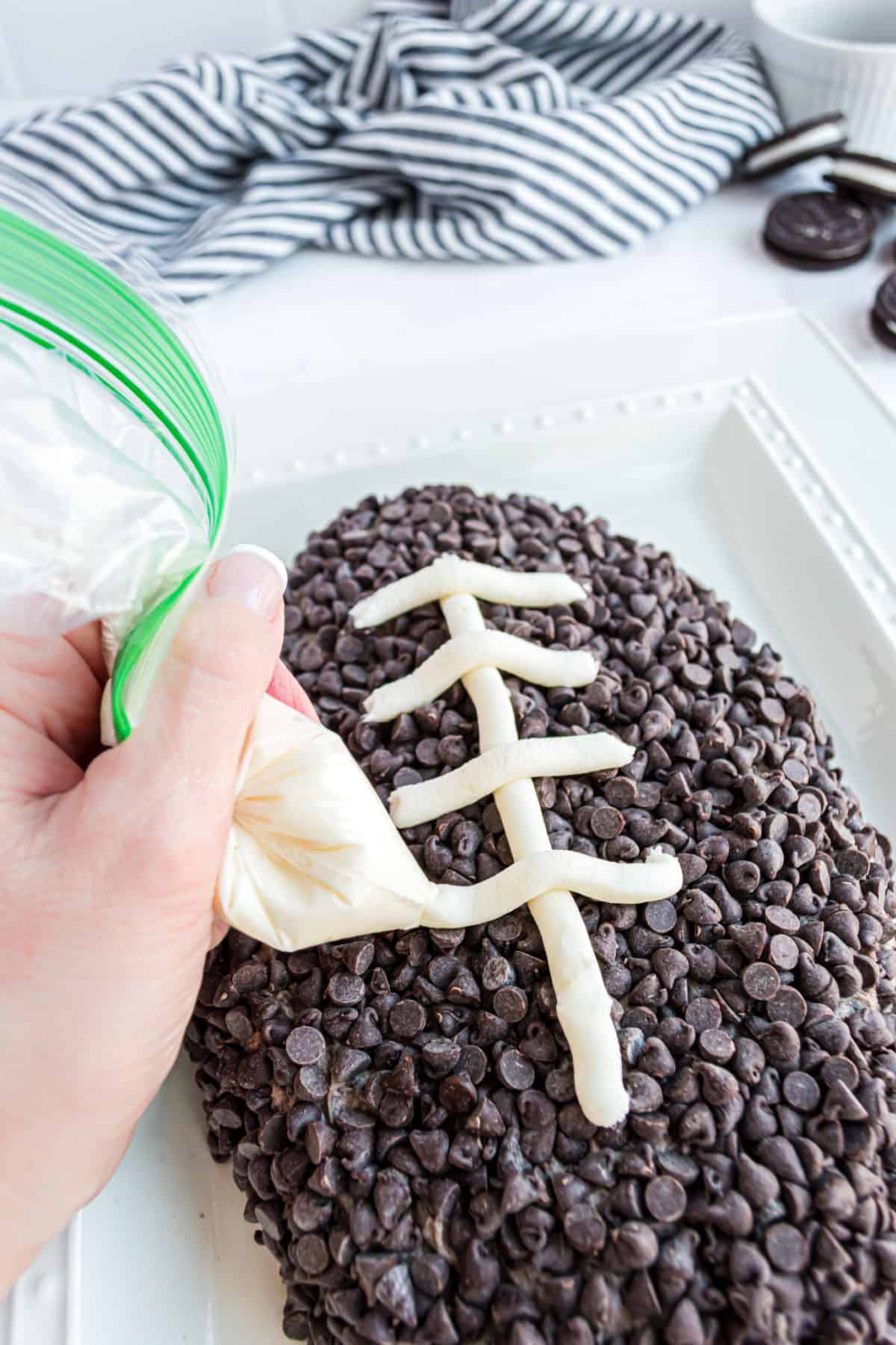 Laces made from cream cheese filling being piped onto football shaped cheese ball.