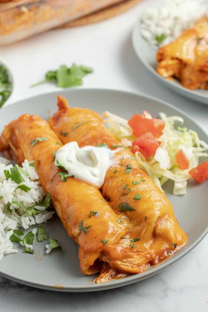 Two chicken enchiladas covered in cheese and sour cream on a gray plate.