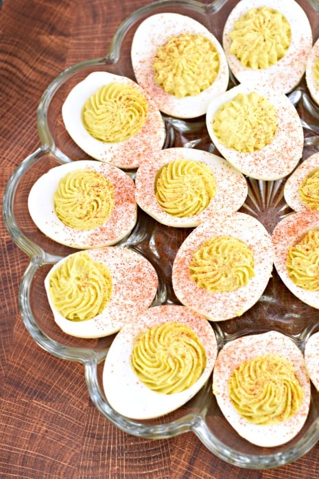 Glass plate filled with hard boiled eggs, cut in half and filled with deviled egg filling.