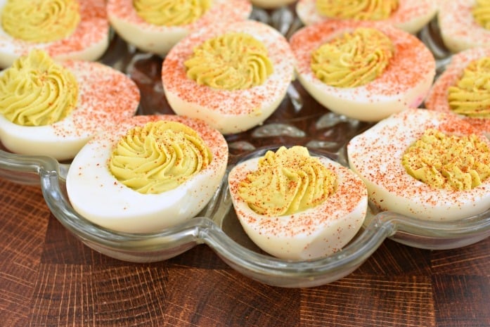 Glass plate filled with deviled egg halves topped with paprika.