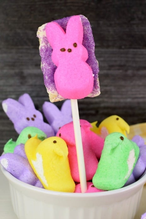 Bowl of marshmallow Peeps and one rice krispie treat on a stick with purple sugar and a pink bunny PEEP.