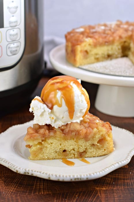 Big slice of apple cake with Instant Pot in background, Slice of apple cake is topped with ice cream and caramel sauce.