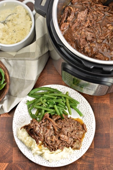 Top view of Instant Pot with balsamic shredded beef, plate with beef, mashed potatoes and green beans.