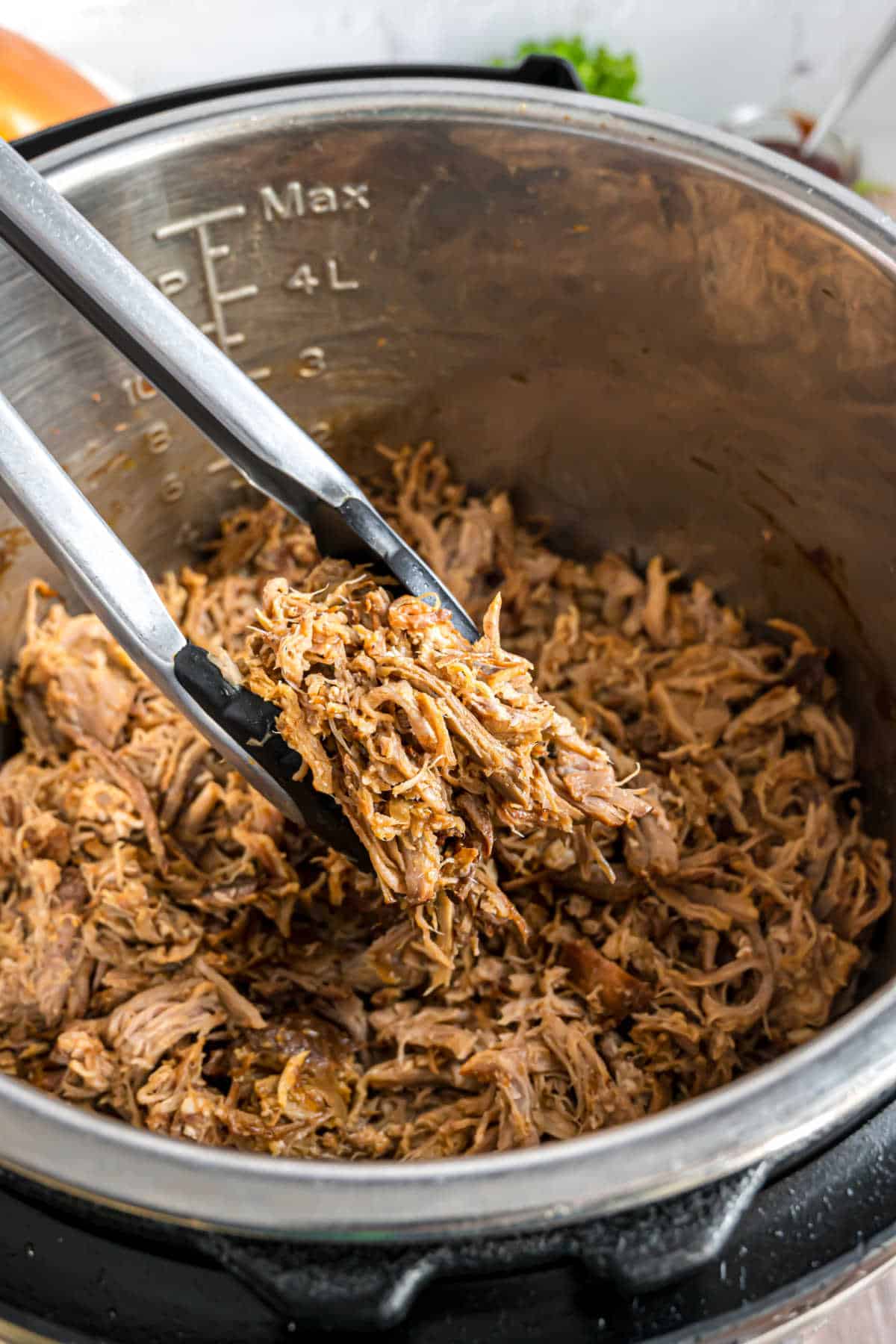 Shredded pork in the Instant Pot with tongs pulling it up.