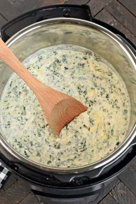 Instant Pot filled with spinach artichoke dip and wooden spoon.