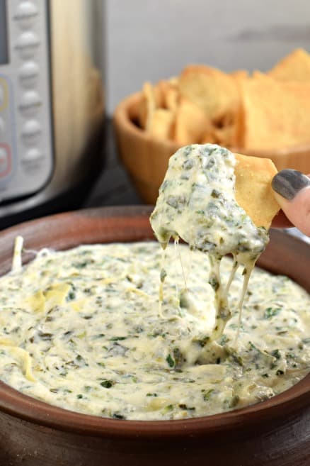 Bowl with spinach artichoke dip and big scoop on a pita chip. 