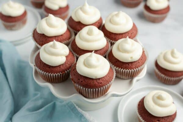 Red velvet cupcakes on a white cake plate with swirls of cream cheese frosting.