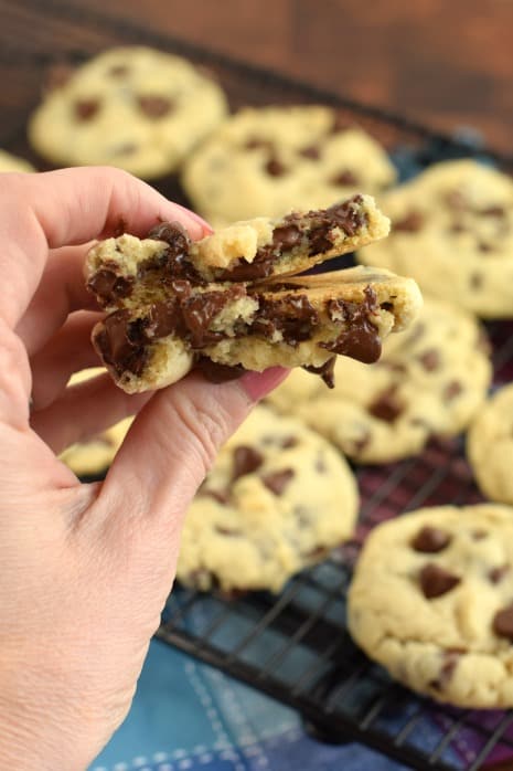 Hand holding broken soft batch chocolate chip cookie with warm chocolate chips.