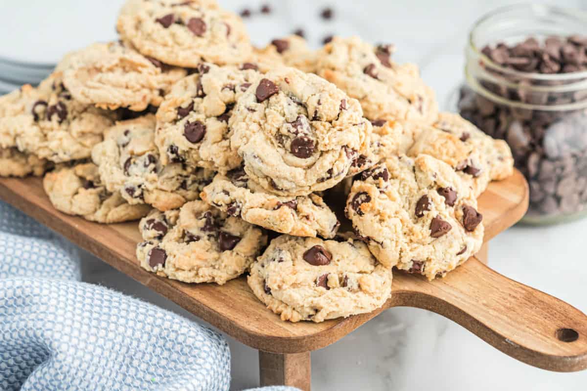 Chocolate chip cookies stacked on a wooden cutting board.