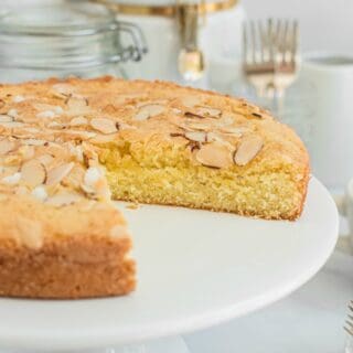 Almond cake on a white cake platter with a slice removed.